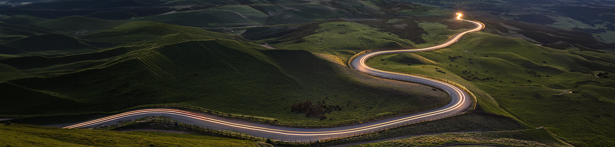 Aerial view of a winding road with light trails through green hills