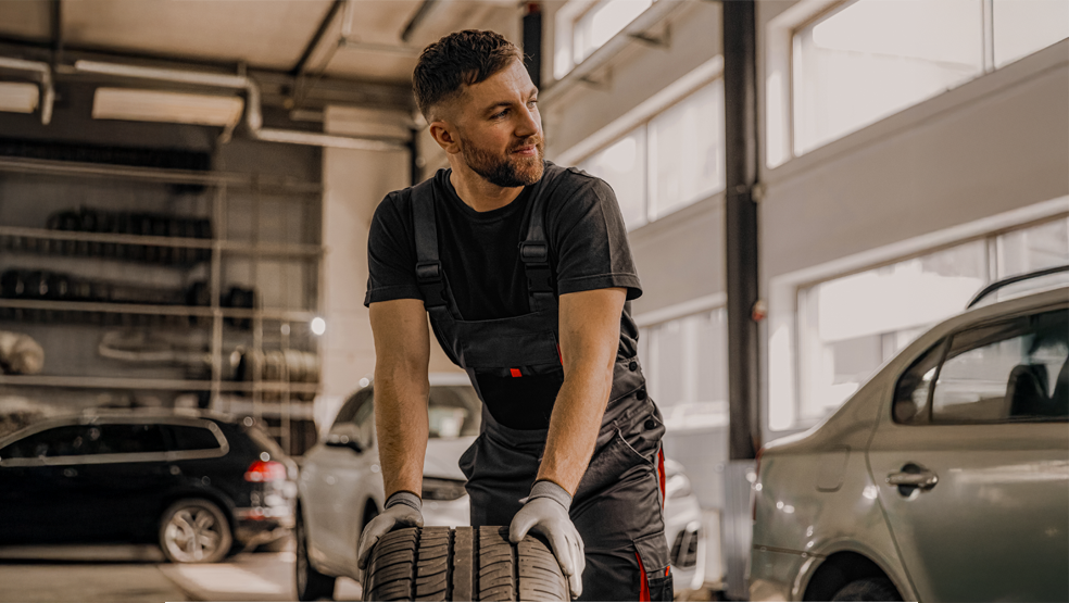 Car mechanic rolls a tire through the workshop