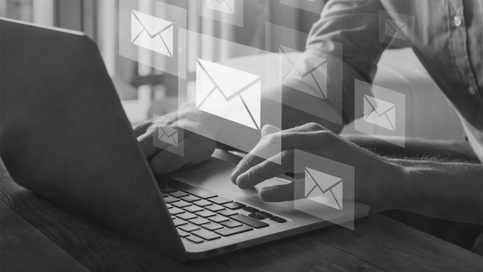 Black and white picture of a person writing emails on a laptop