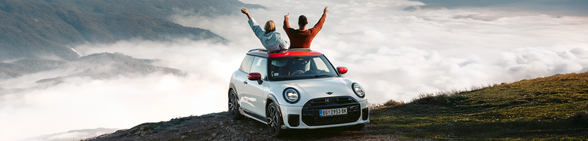 BMW MINI car with two people enjoying a mountain view above the clouds.
