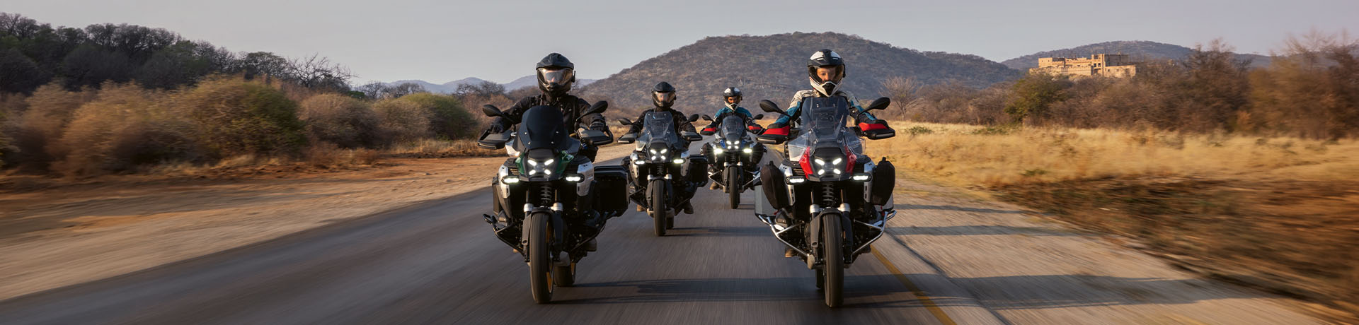 Four BMW motorcyclists riding BMW motorcycles on a scenic road with mountains in the background.