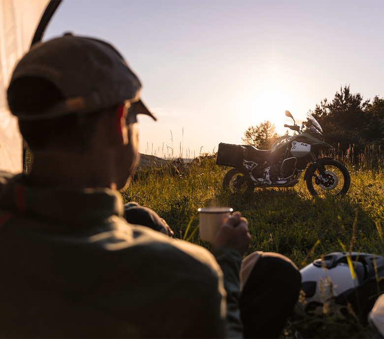 A person relaxing and enjoying the view of a BMW motorcycle at sunset.